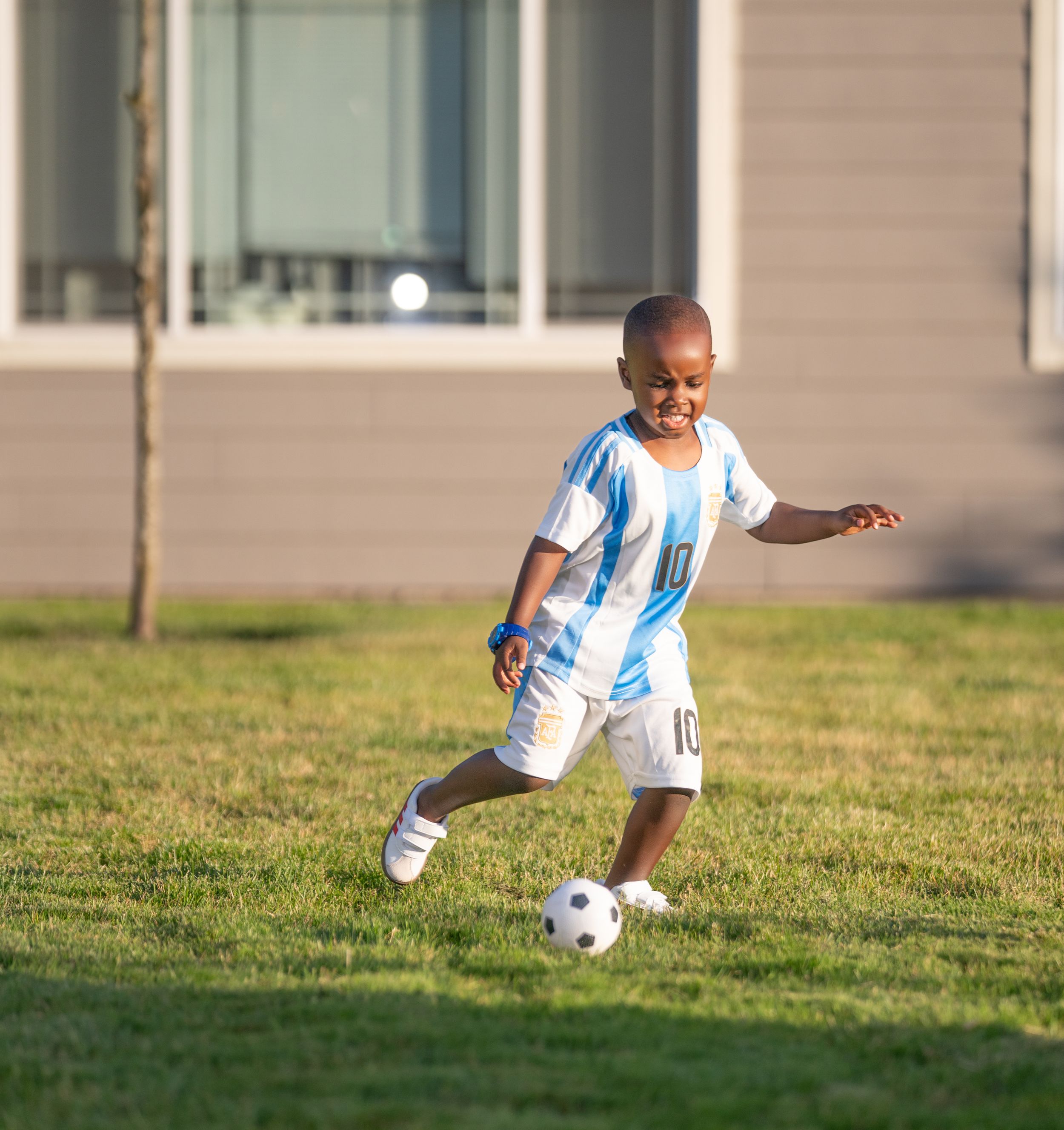 Young soccer player practices dribbling skills on a grassy field in late afternoon sunlight.