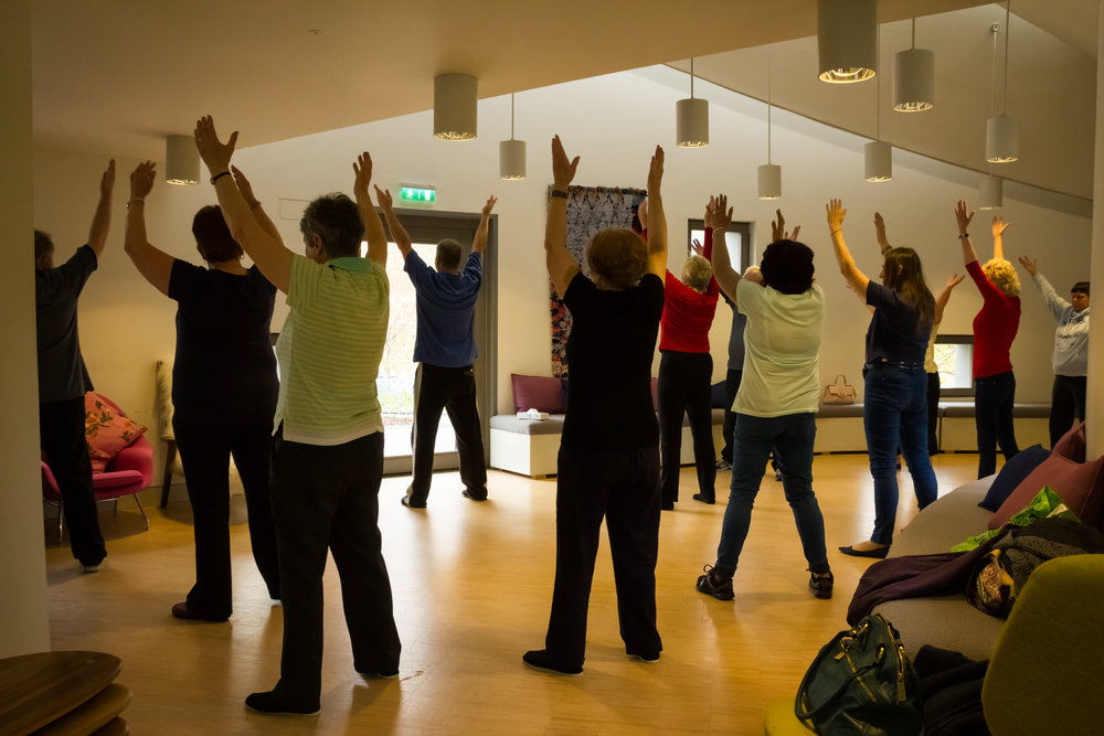 People participating in a group exercise class with raised arms in a mirrored studio space.