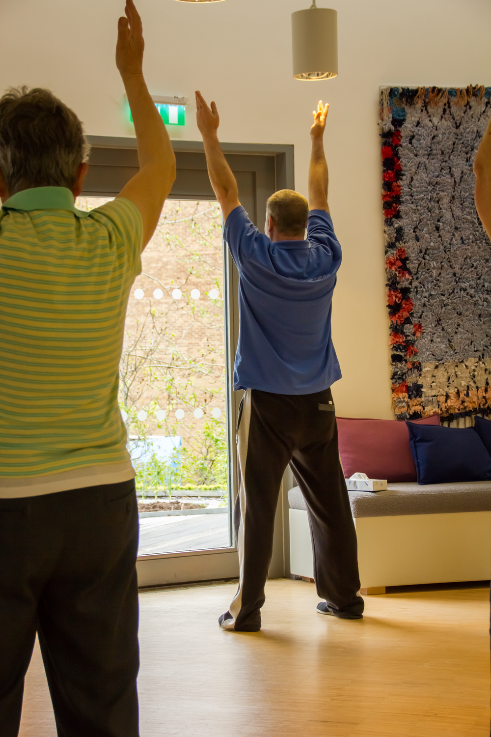 Two people standing in an exercise studio with raised arms near a window.