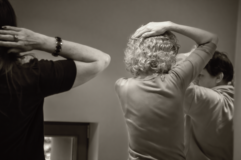 Three people stretching their arms behind their heads in a dance studio.