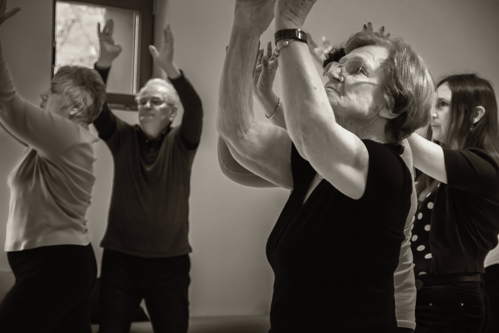 People participating in a dance or exercise class with arms raised in black and white.