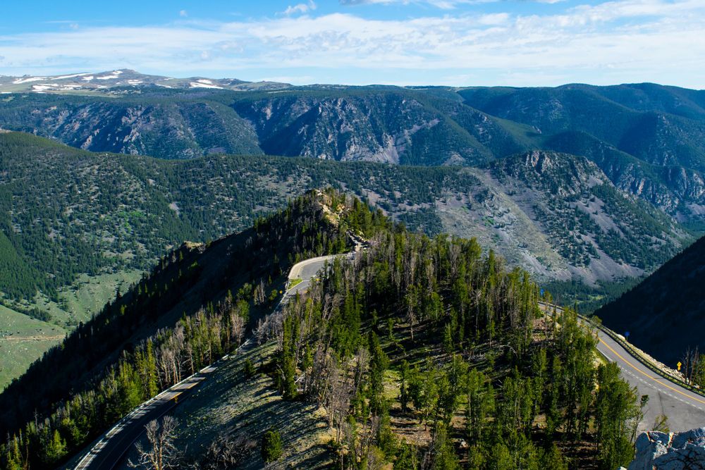 Aerial view of forested mountain valley with winding roads and steep cliffs.