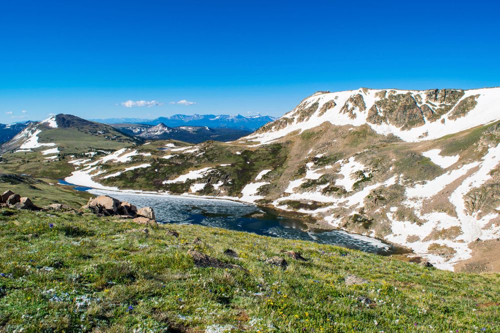 Dramatic mountain landscape with snow patches and alpine lakes under bright blue skies.