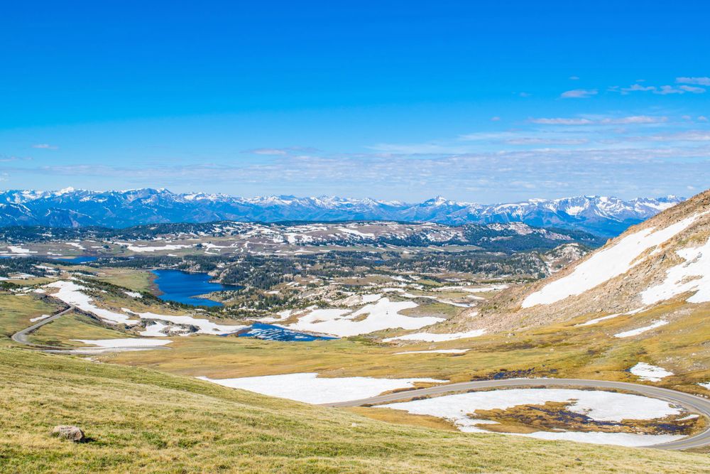 Panoramic view of alpine lakes and snow-covered peaks stretching across a mountain range.