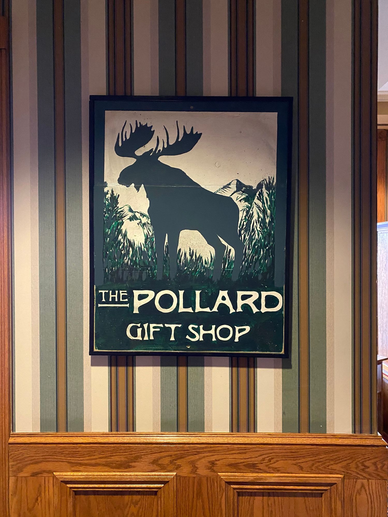 Vintage-style moose silhouette sign for The Pollard Gift Shop against striped wallpaper.