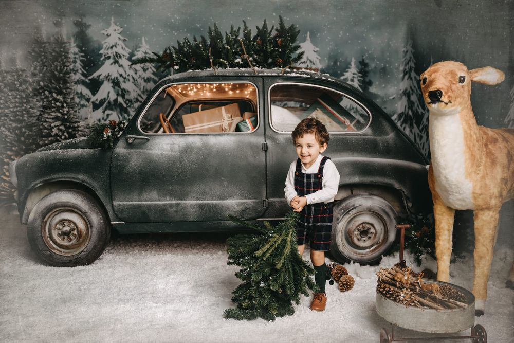 Vintage holiday scene with classic car, decorated Christmas tree and large stuffed reindeer.