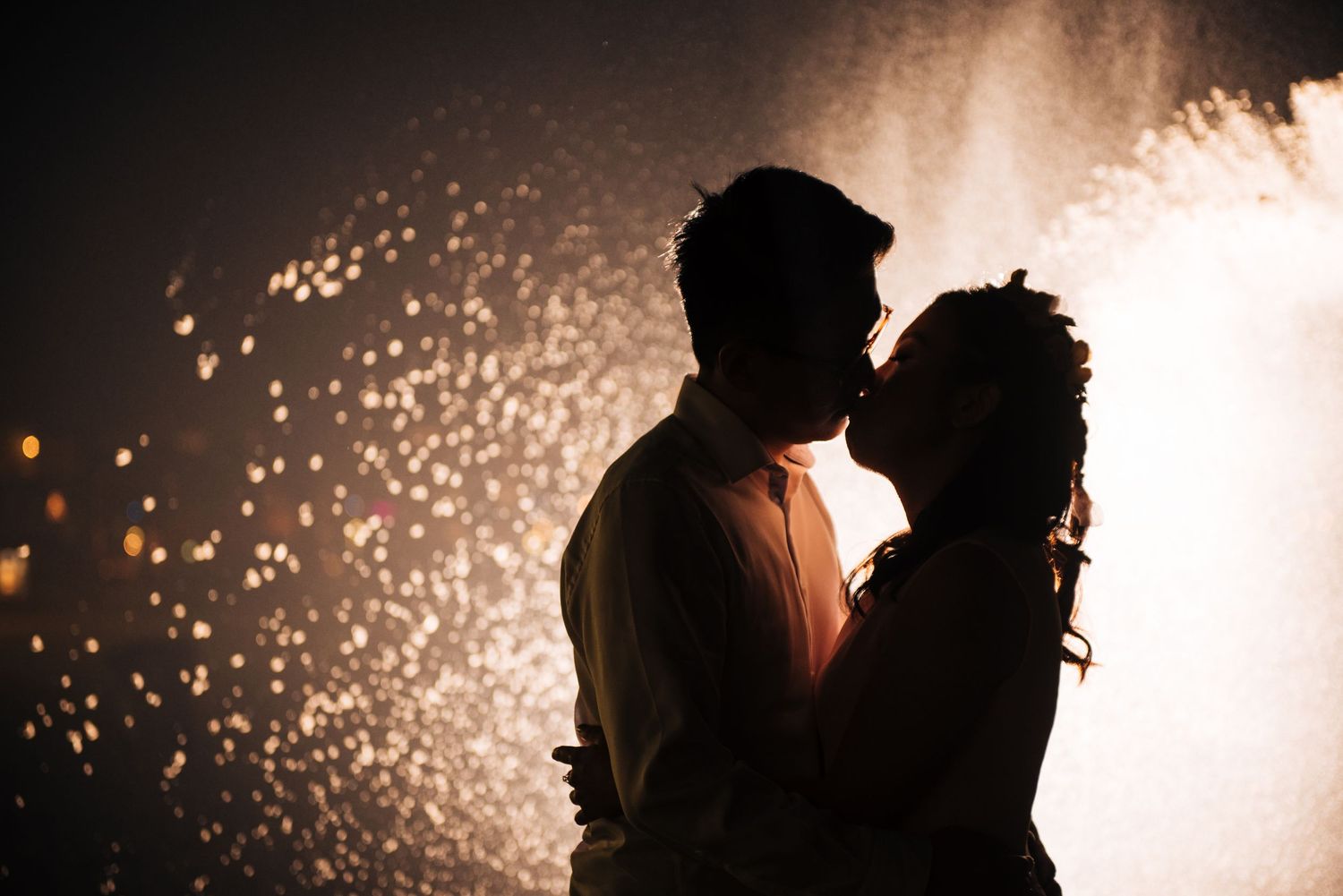 A couple's silhouette against sparkling fireworks at night.