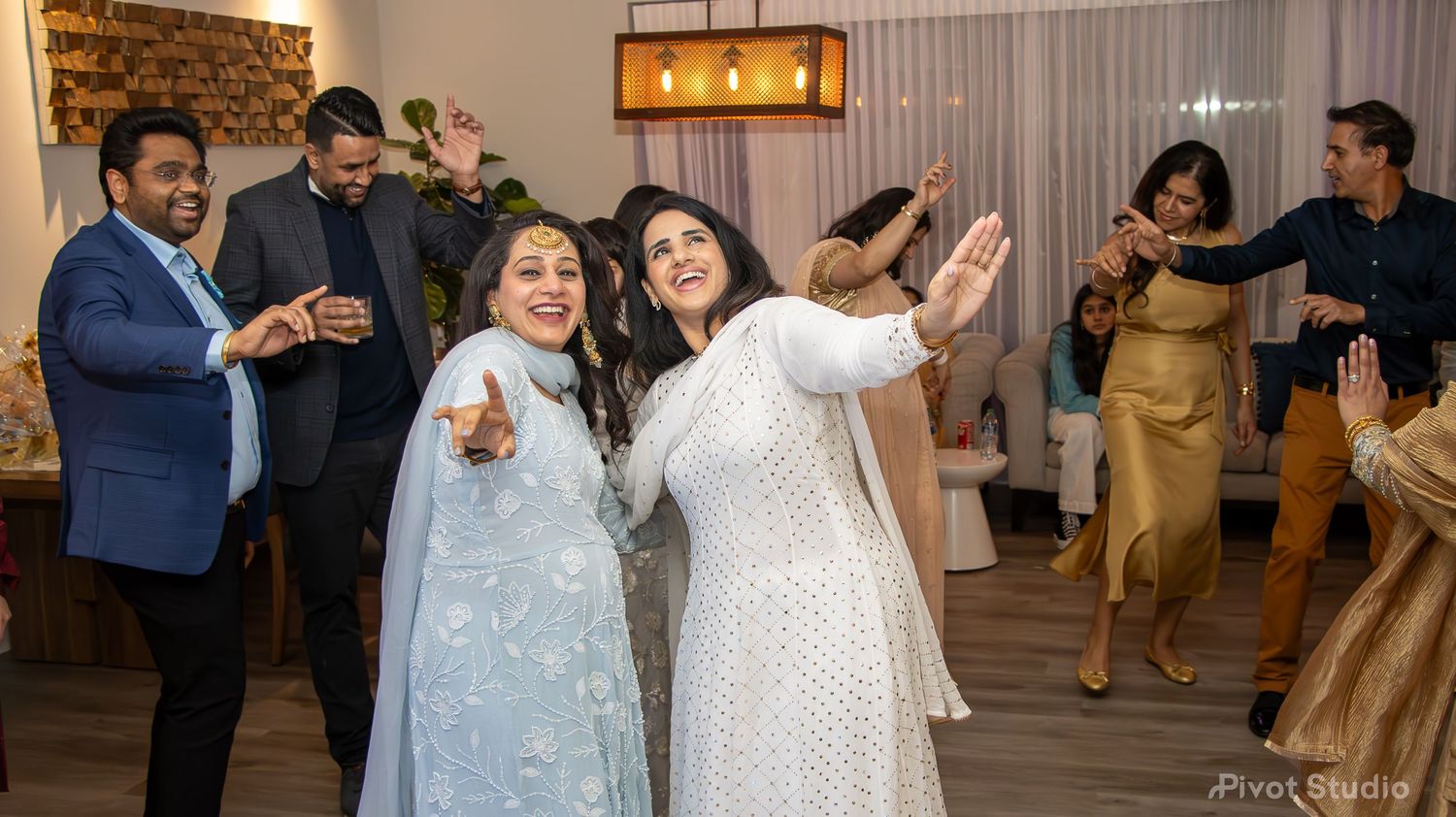 Group of South Asian guests dancing joyfully at an indoor celebration party event.