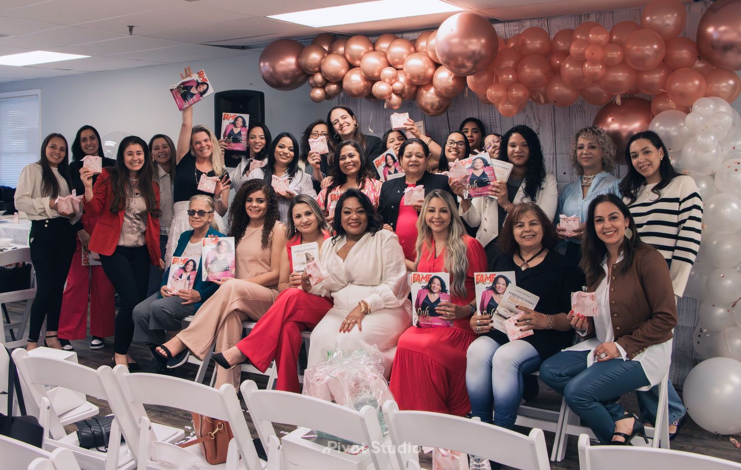 Large group of women holding magazines at a rose gold themed indoor celebration event.