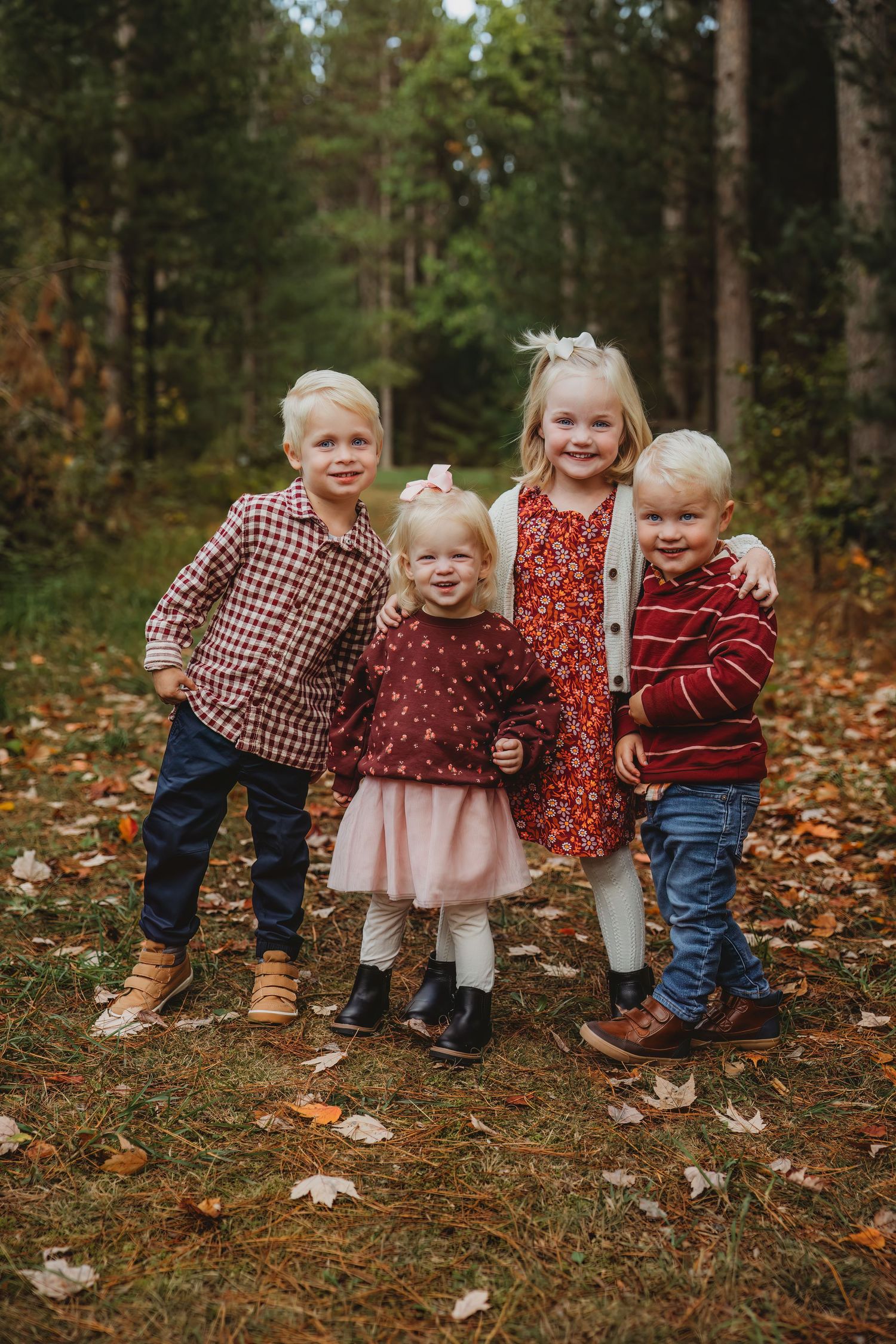 Four young children in fall outfits playing together among autumn leaves.