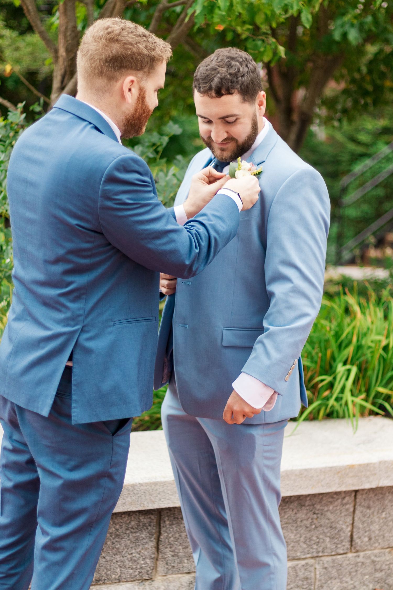 Groomsman helps adjust another's boutonniere before the wedding ceremony.