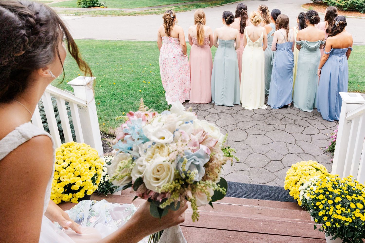 Wedding party in pastel dresses gathering outdoors with yellow mums.