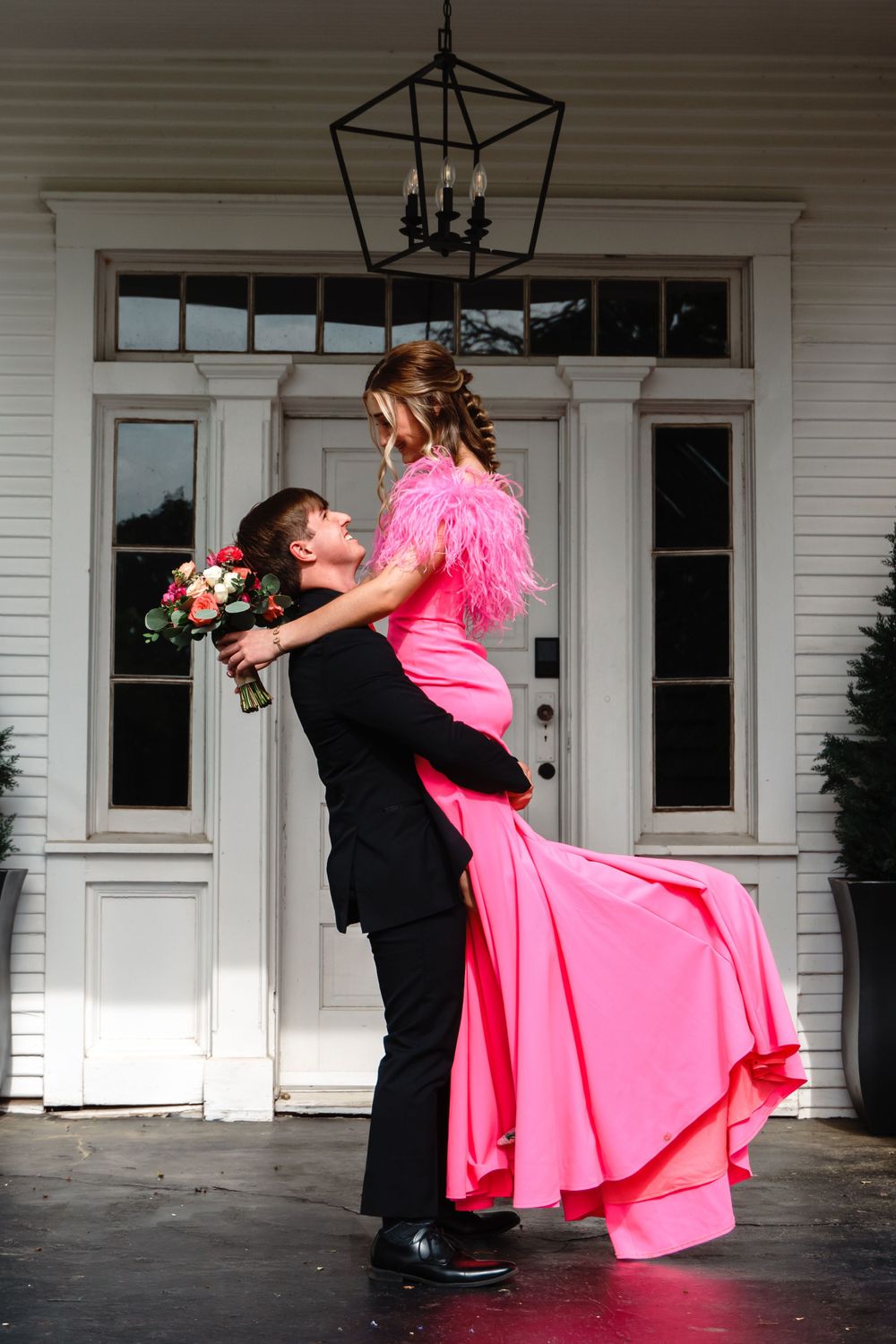 Couple in formal attire sharing a playful lift pose, her pink dress flowing dramatically.