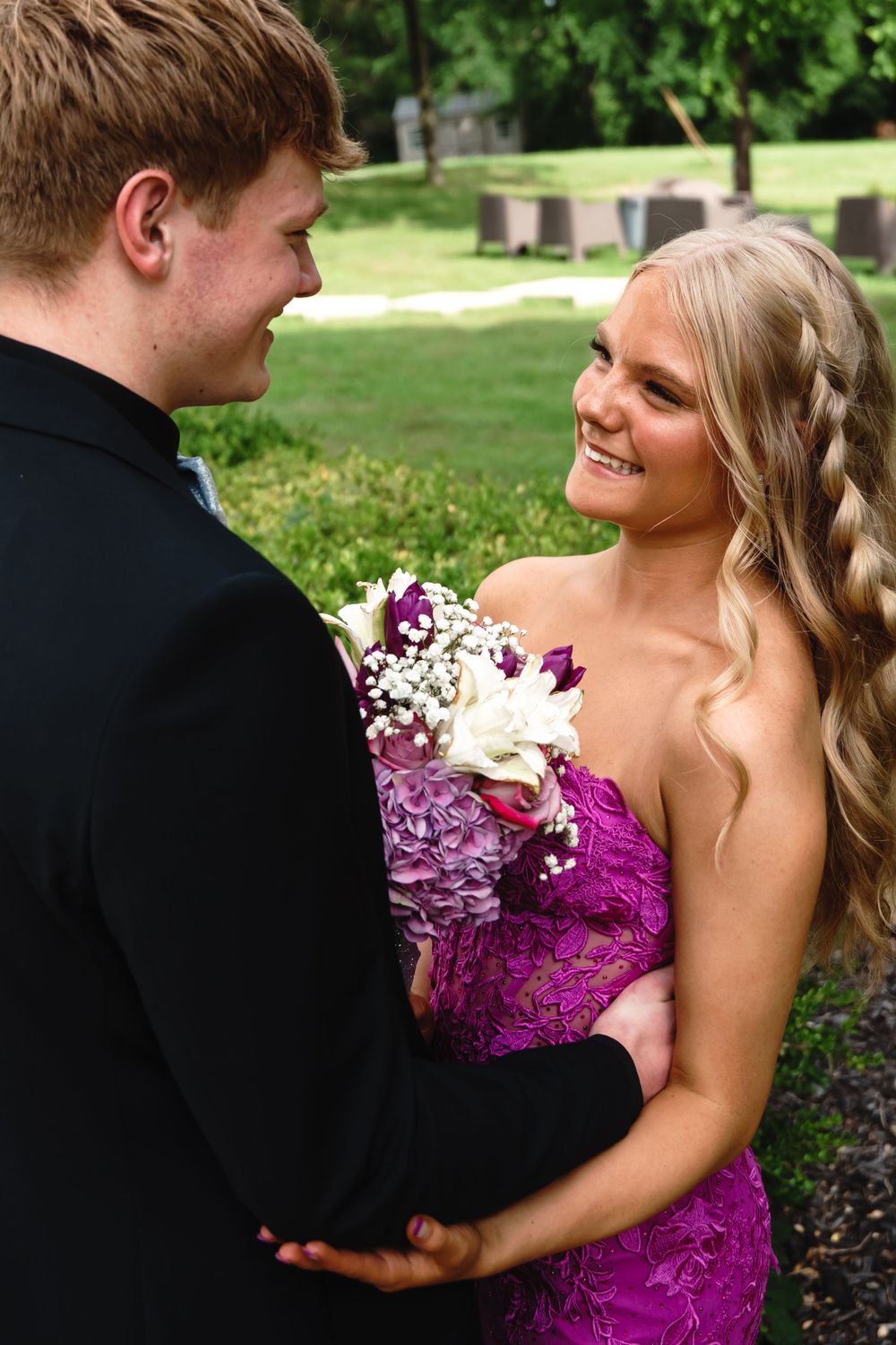Intimate moment captured between couple in formal wear with purple floral bouquet.