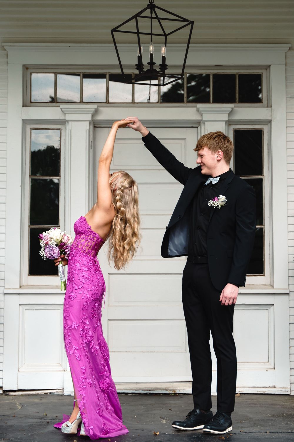 Couple in formal attire performs elegant dance pose in front of white porch entrance.