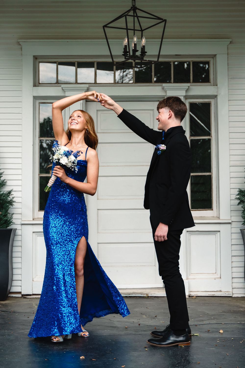 Couple in formal attire dancing together on a porch, with the woman wearing a sparkly blue gown.