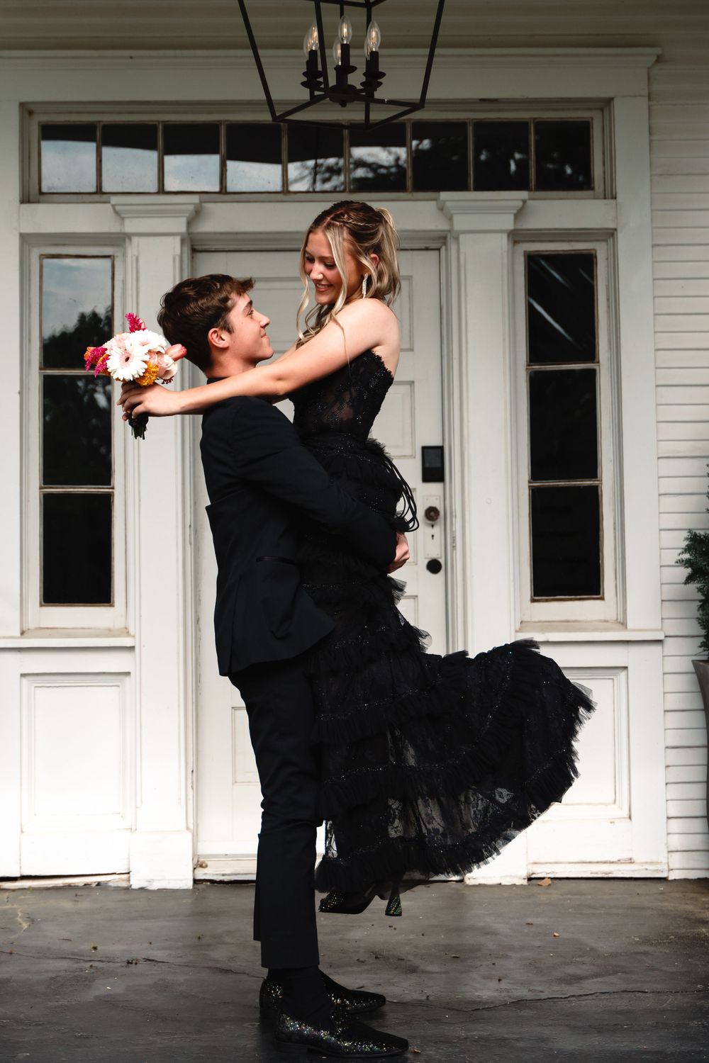 Couple in formal wear sharing a romantic lift pose in front of white double doors.
