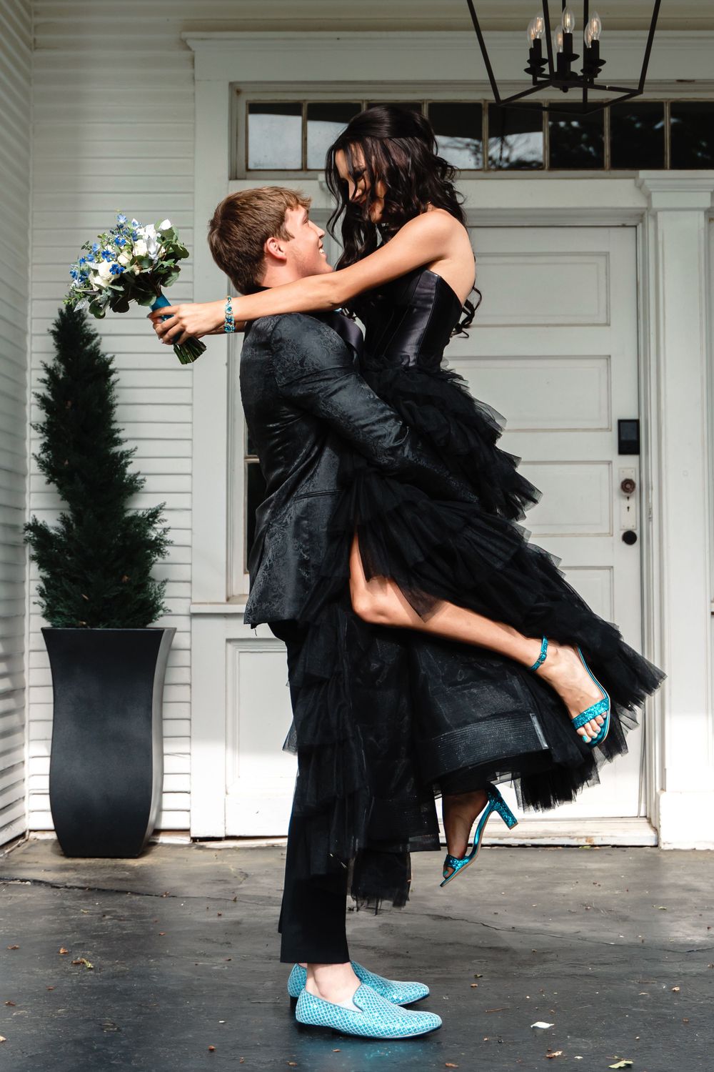 Couple in black attire dancing, with turquoise shoes adding a pop of color against white doors.