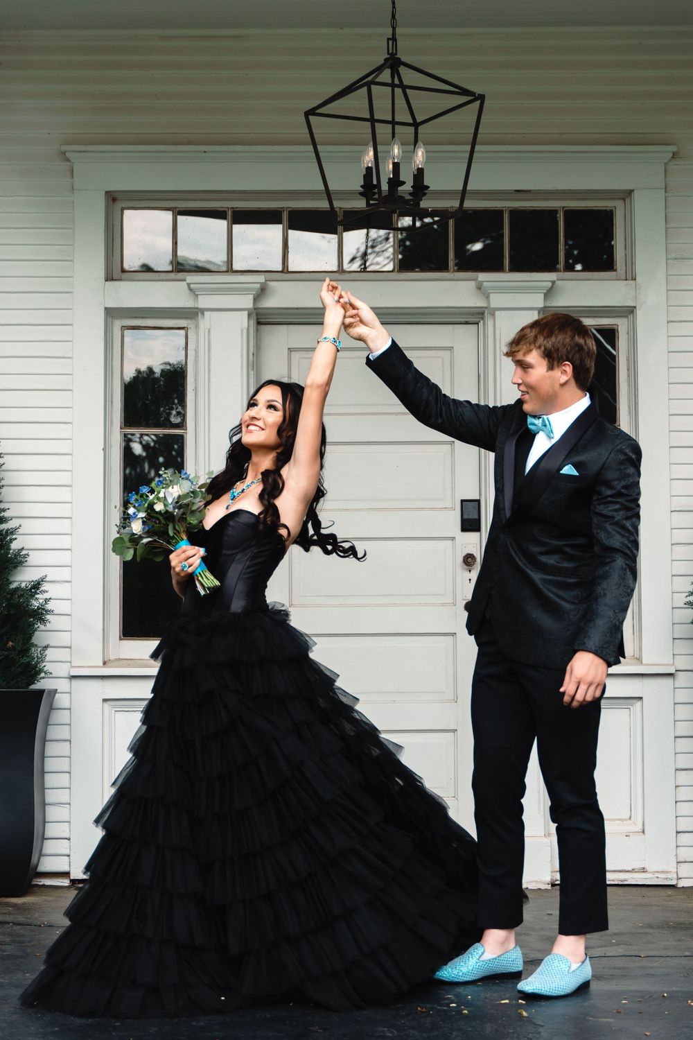 Formal couple dancing on porch, with striking contrast between black gown and blue shoes.