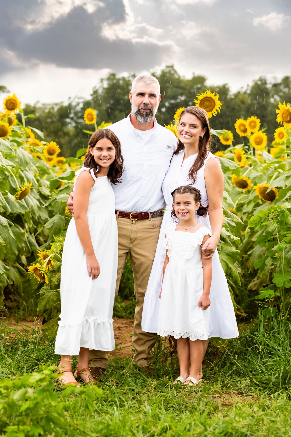 A family poses together in front of a vibrant sunflower field during a summer photo session.
