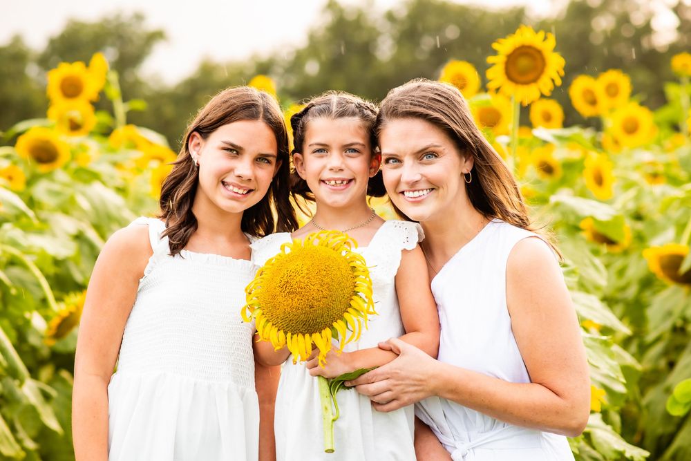 A group wearing white poses for photos in a vibrant sunflower field during golden hour lighting.