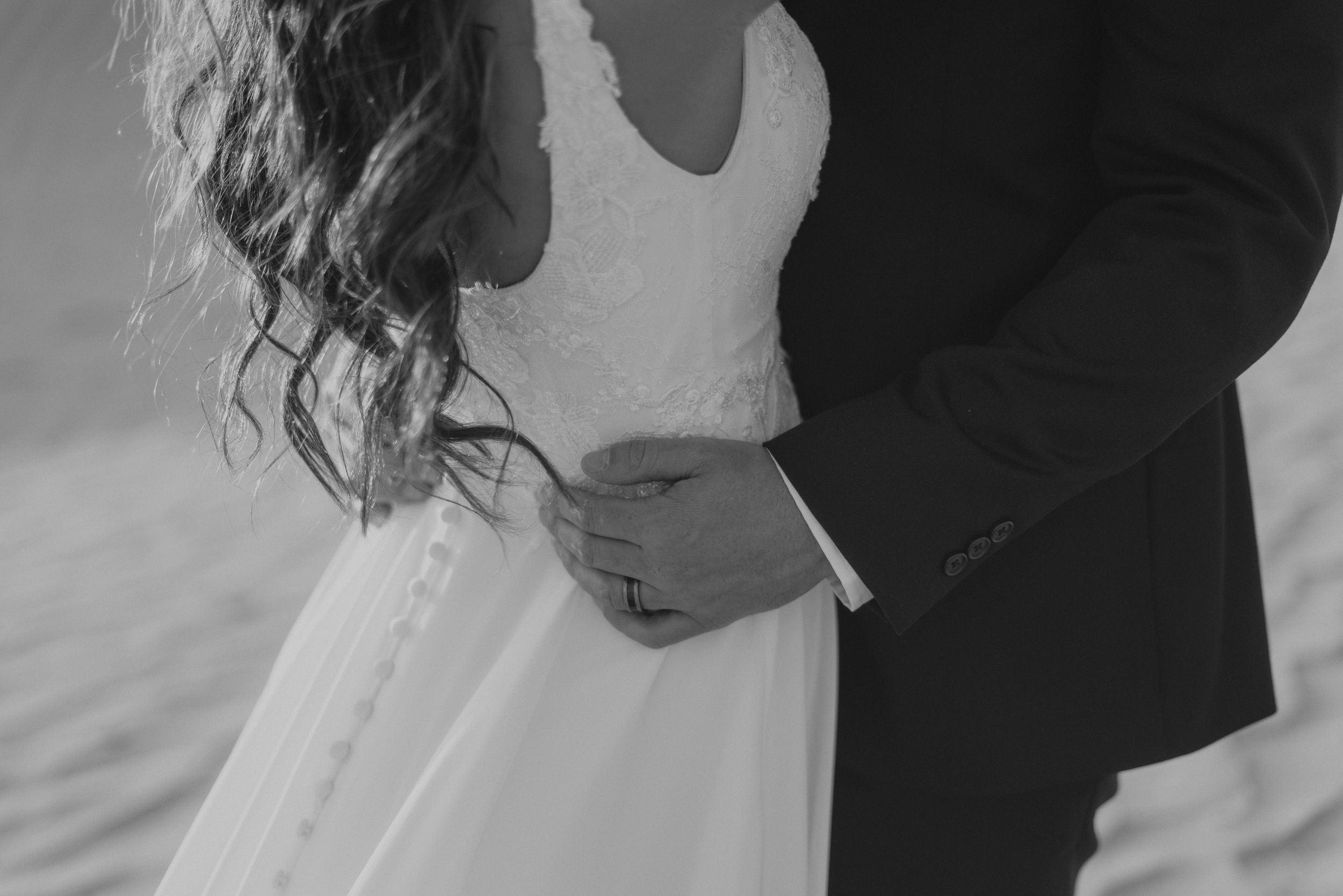 Intimate black and white detail shot of couple's embrace in wedding attire.