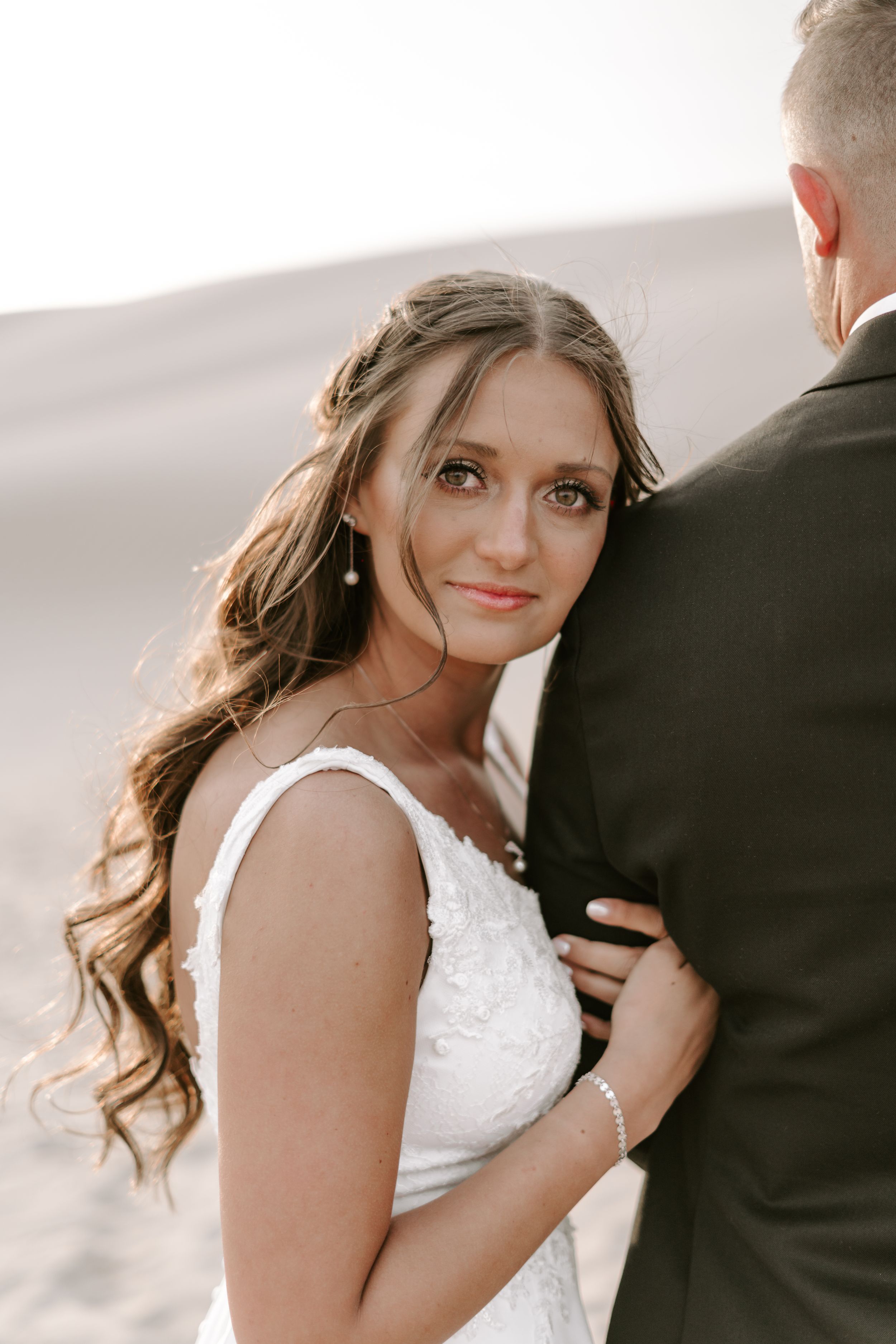 Romantic desert wedding portrait with flowing dress against sandy backdrop.