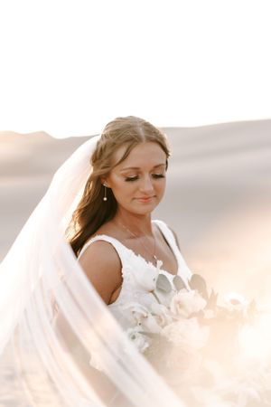 Ethereal bridal portrait in soft sunlight against desert sand dunes with flowing veil.