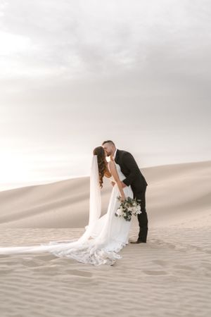 Wedding couple sharing intimate moment in golden light on desert sand dunes.