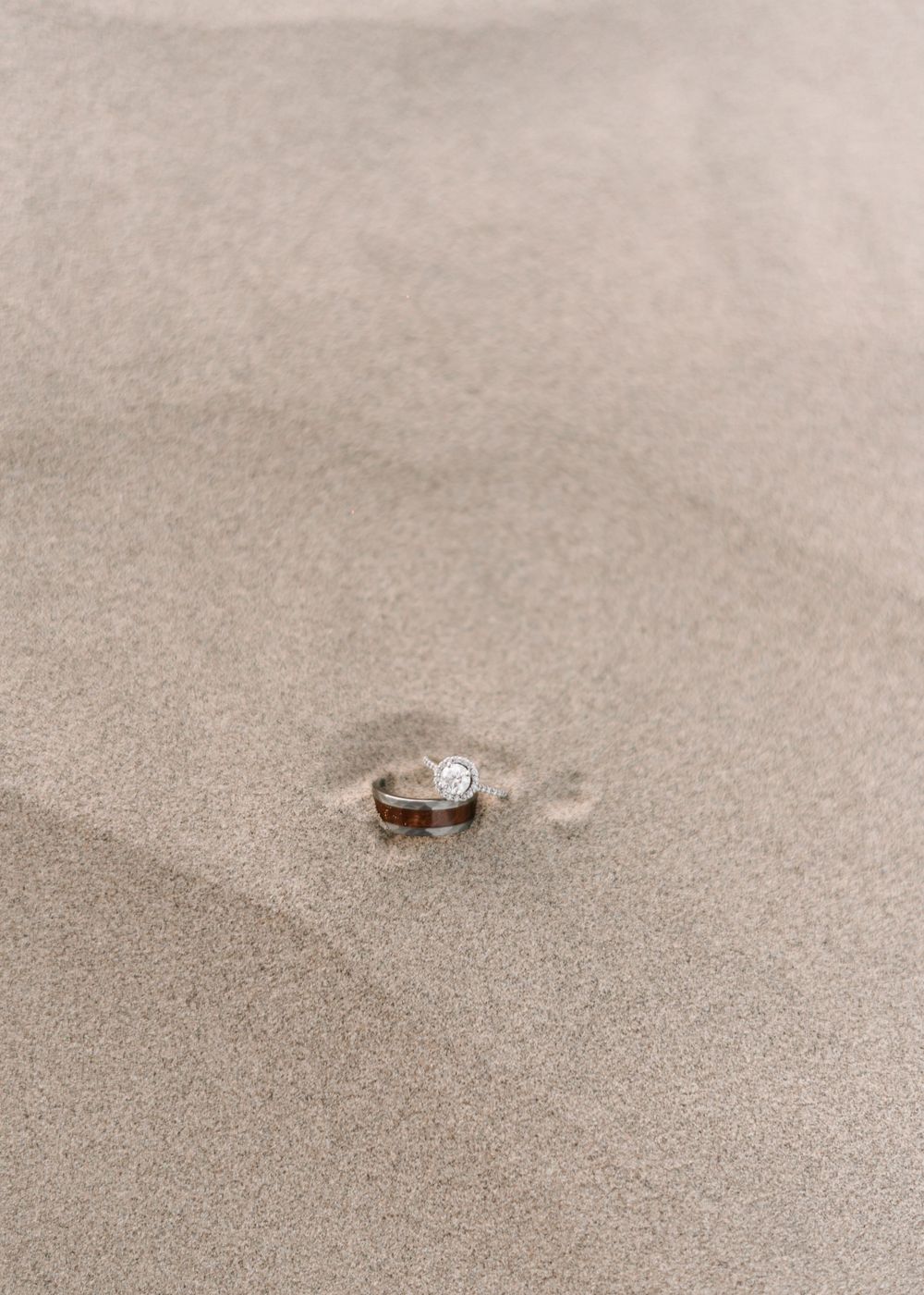 Wedding ring nestled in smooth desert sand creating minimalist composition.