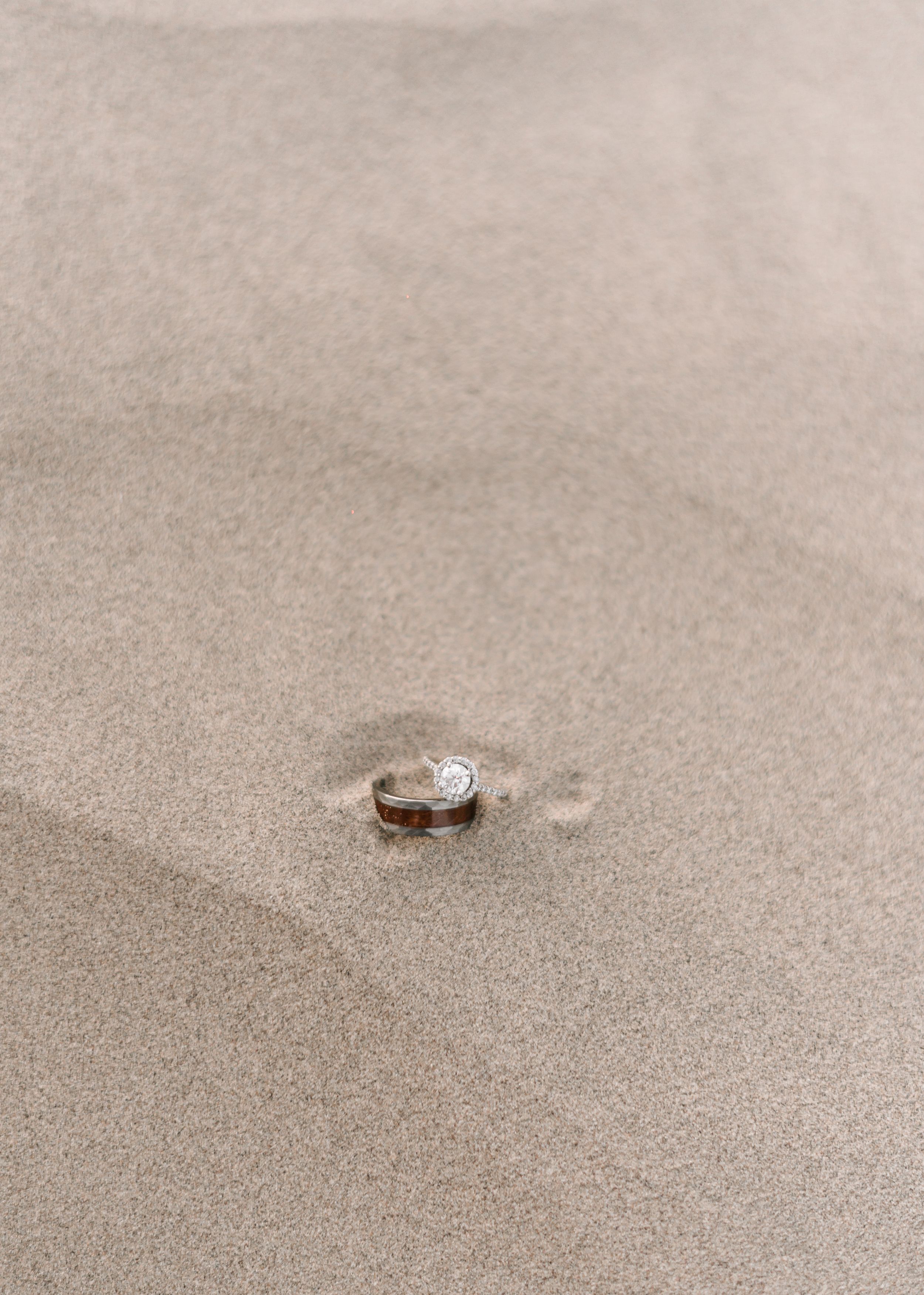 Wedding ring nestled in smooth desert sand creating minimalist composition.
