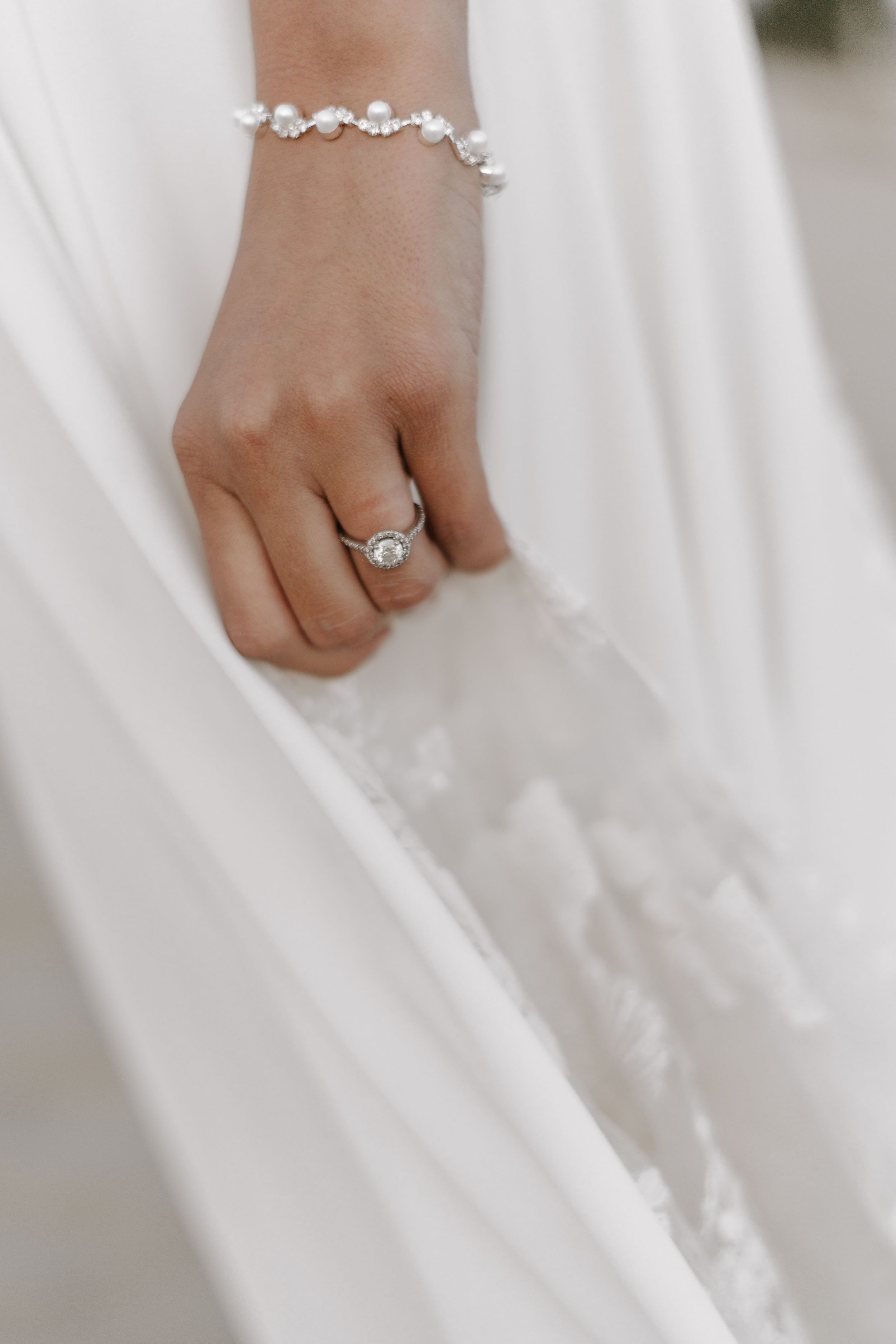 Close-up of delicate bridal jewelry with diamond ring and crystal bracelet.
