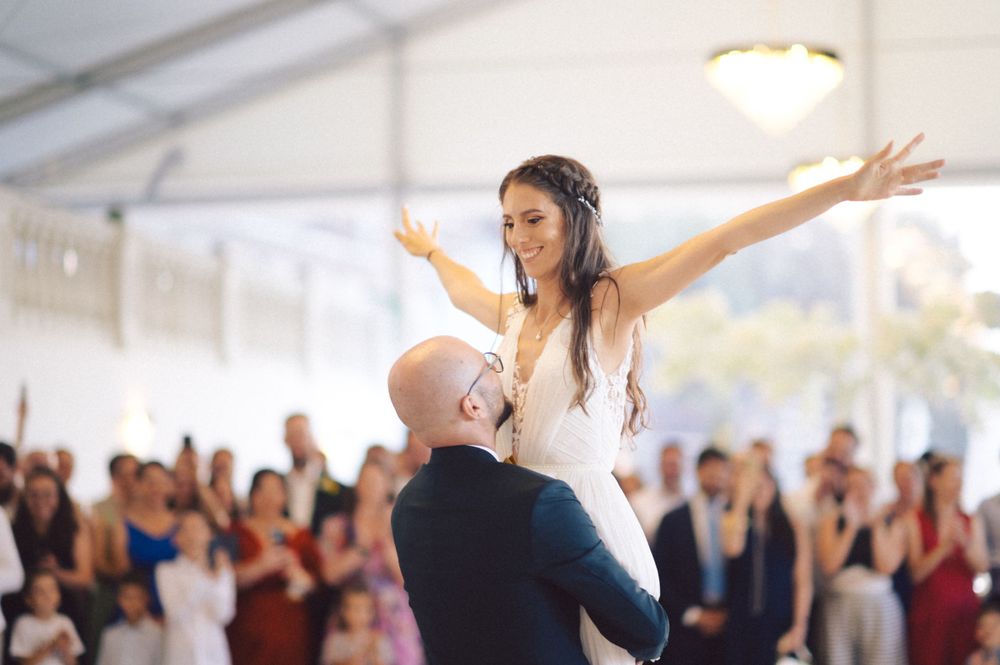 Joyful couple performing an energetic lift during their wedding dance while guests watch.