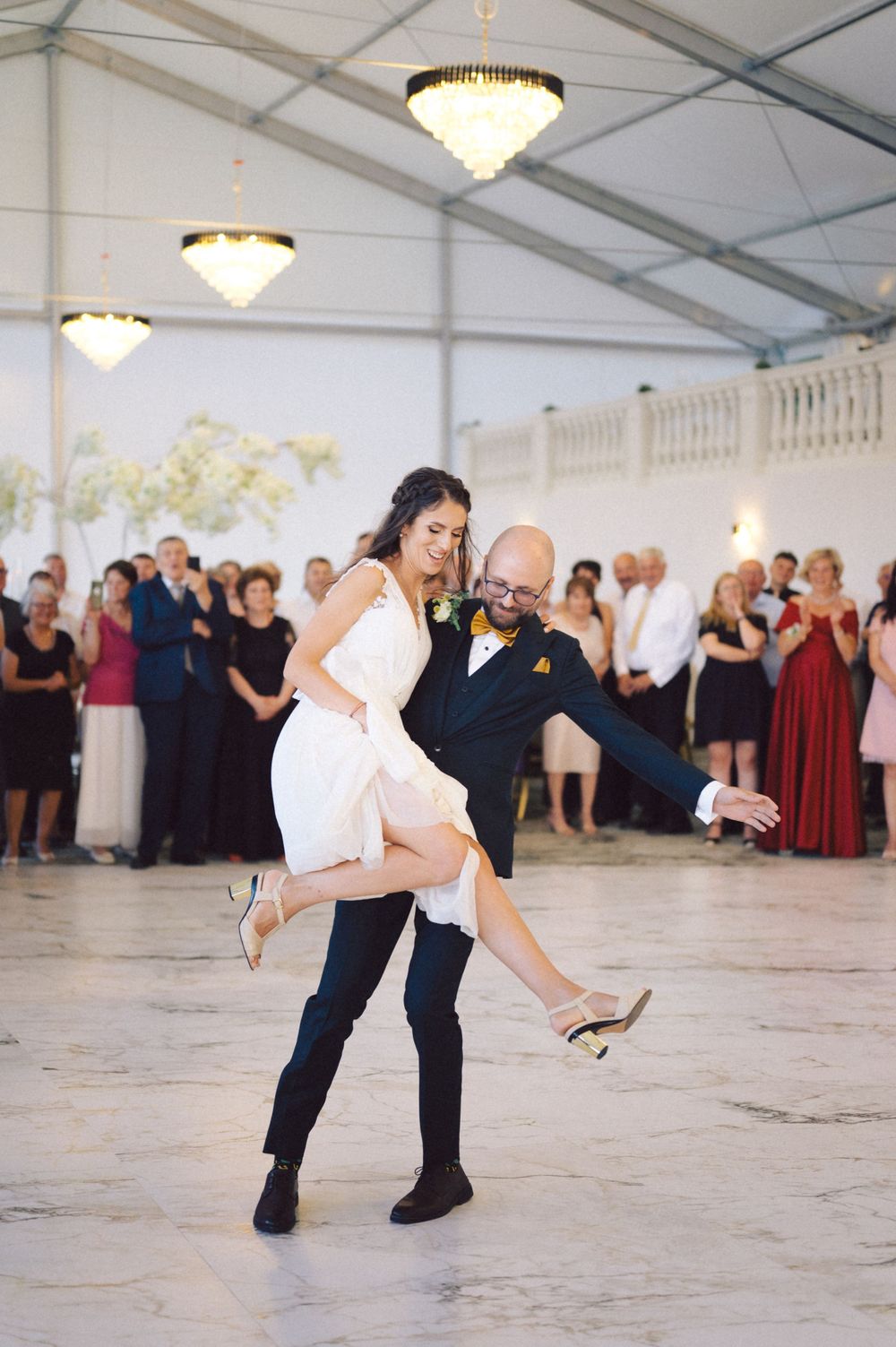 Couple performs dramatic dance move during wedding reception under crystal chandeliers.