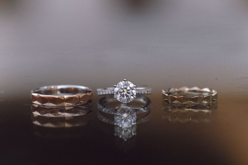 Three wedding rings displayed on a reflective surface showing elegant bands and a diamond solitaire.