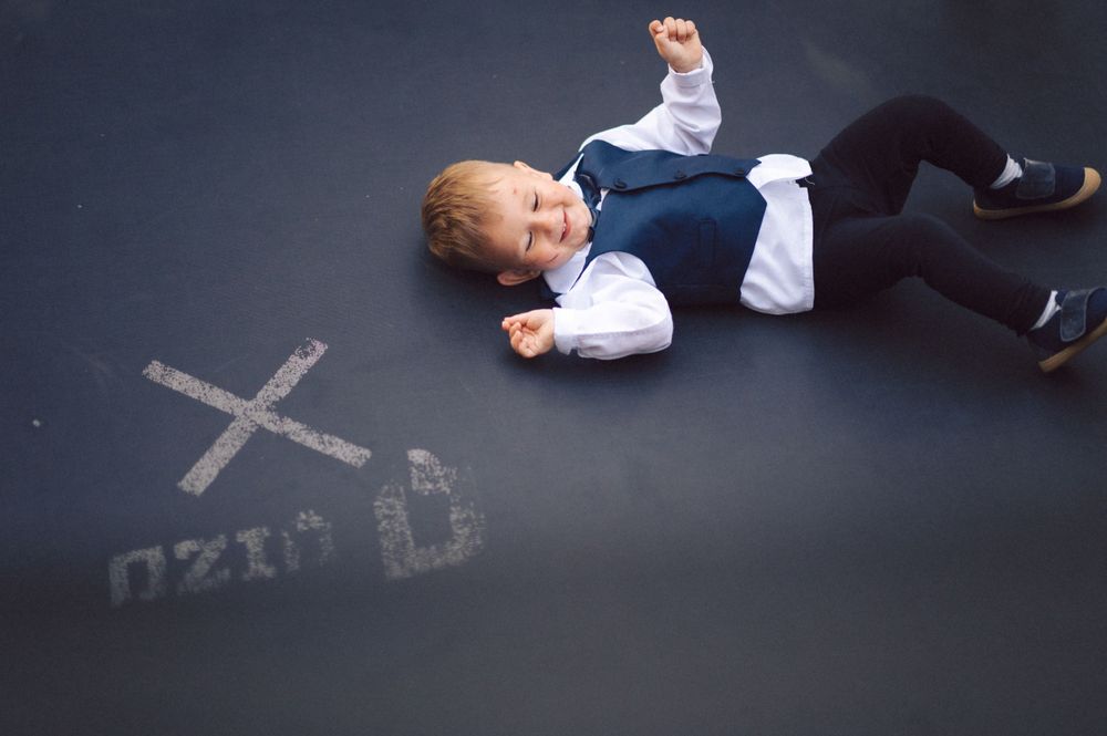Young child in formal attire lying on chalk-drawn ground at an event.