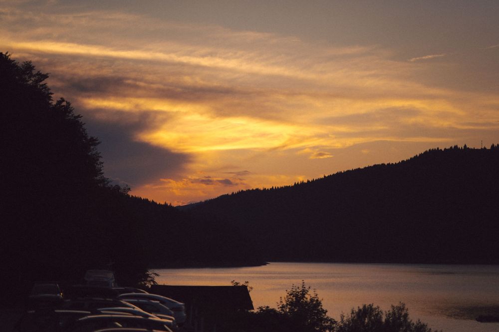 Dramatic orange sunset over a lake with silhouetted mountains and treeline.