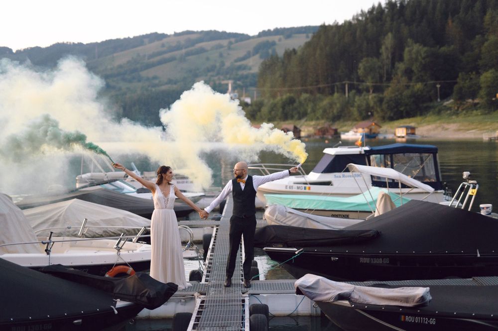 Newlyweds celebrating with smoke flares on a dock surrounded by boats.