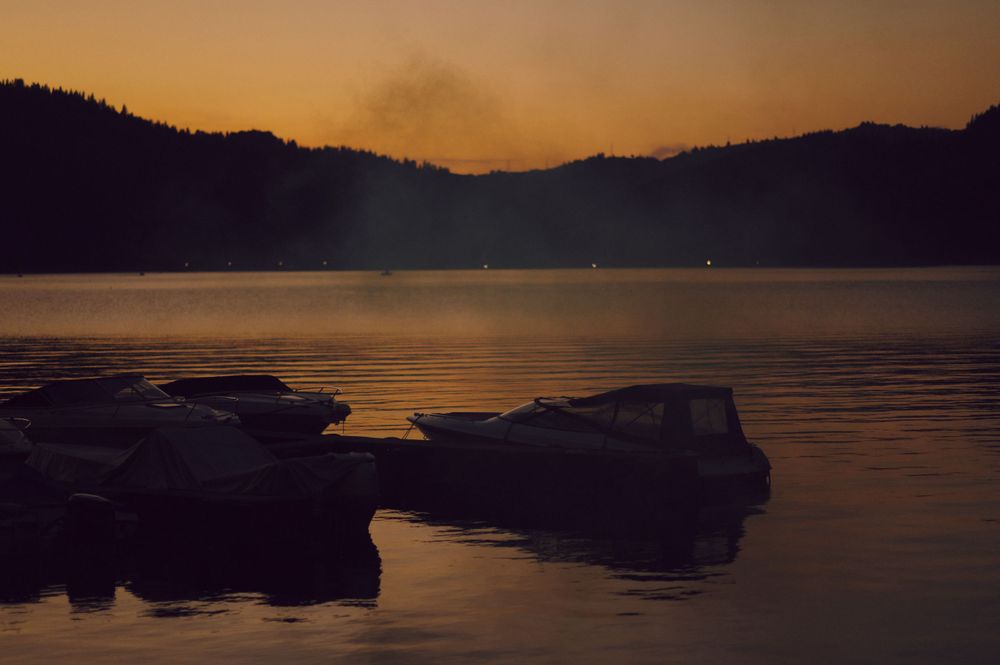 Misty lake at sunset with rocky shoreline silhouetted against orange sky.