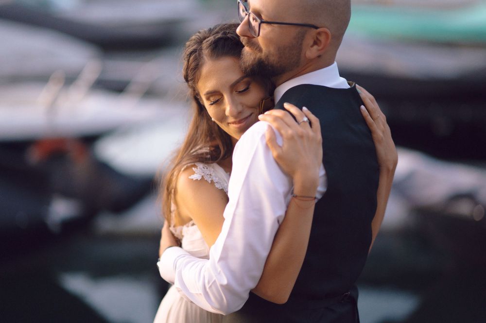 A romantic embrace between a couple by a marina, with the bride wearing a flowing white dress.