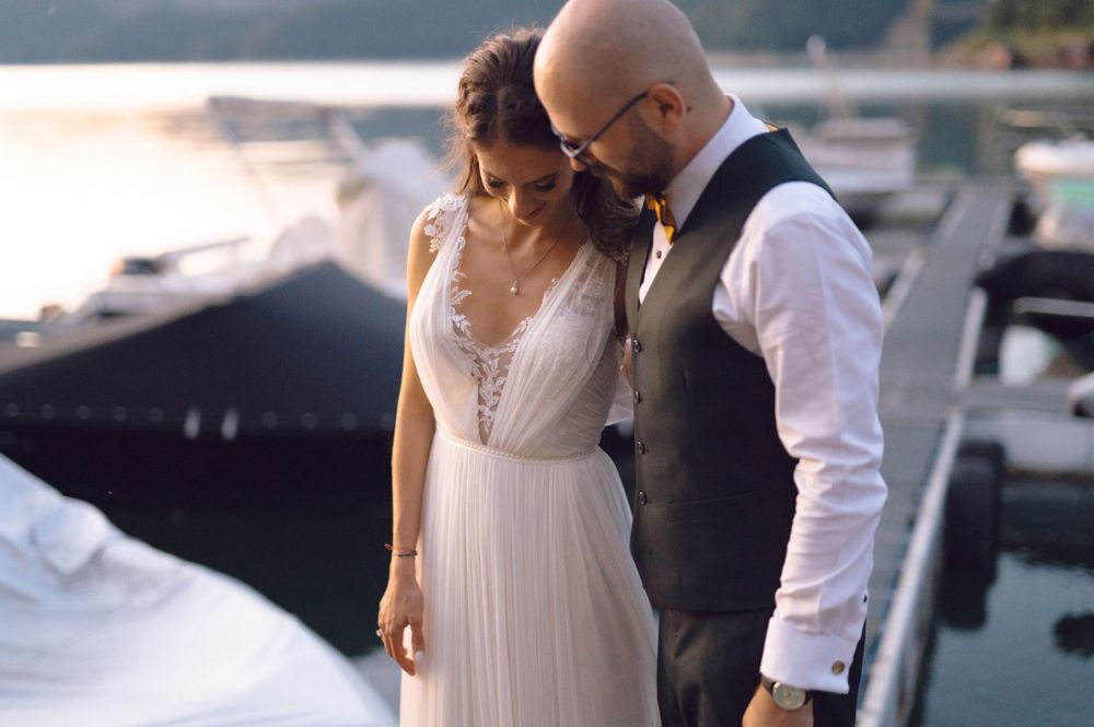 Intimate wedding portrait of a couple in formal attire standing near boats at a marina.