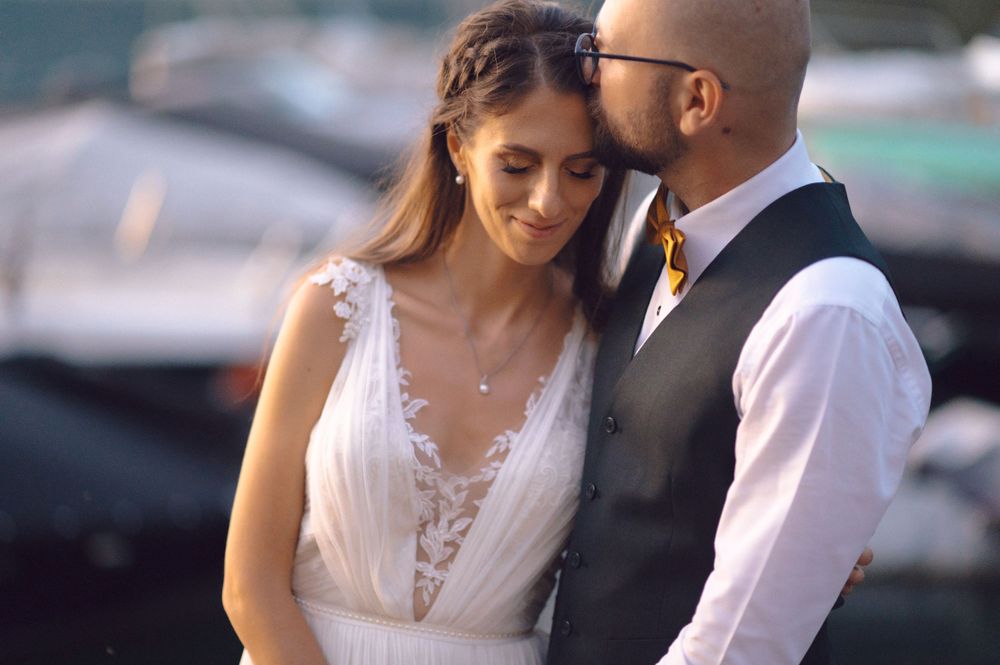 A tender moment between newlyweds, with the bride wearing a delicate lace wedding dress near the water.