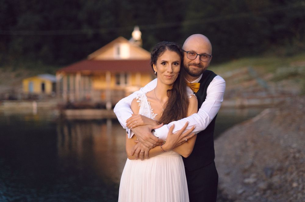 A romantic waterfront wedding photo with a rustic cabin in the background at dusk.