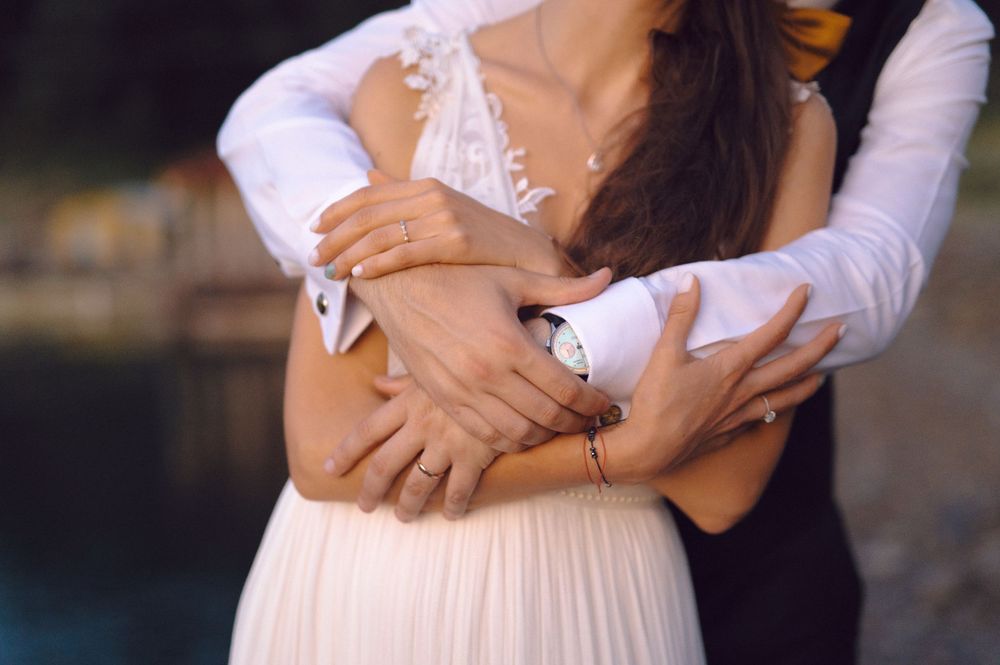 Close-up of embracing hands showing wedding rings against a white flowing dress.