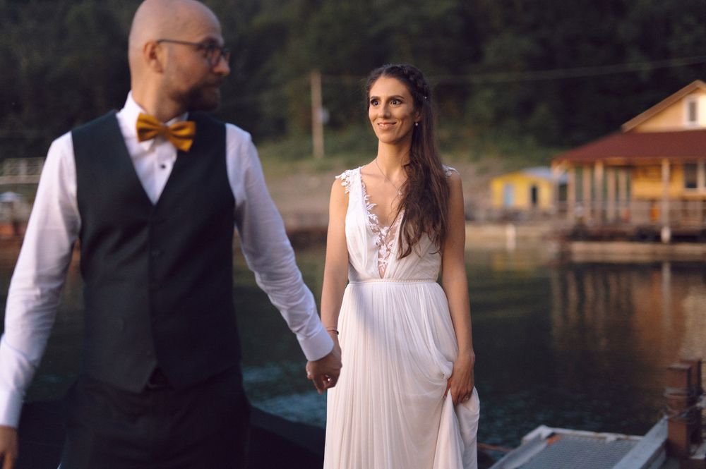 Elegant couple walking hand in hand along a waterfront dock in wedding attire.