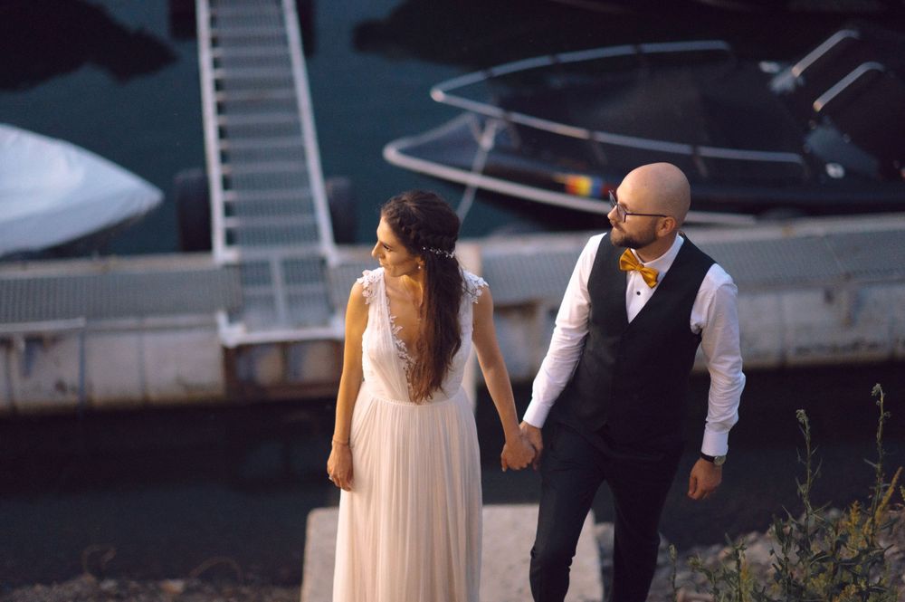 Wedding couple walking down a marina dock holding hands at twilight.