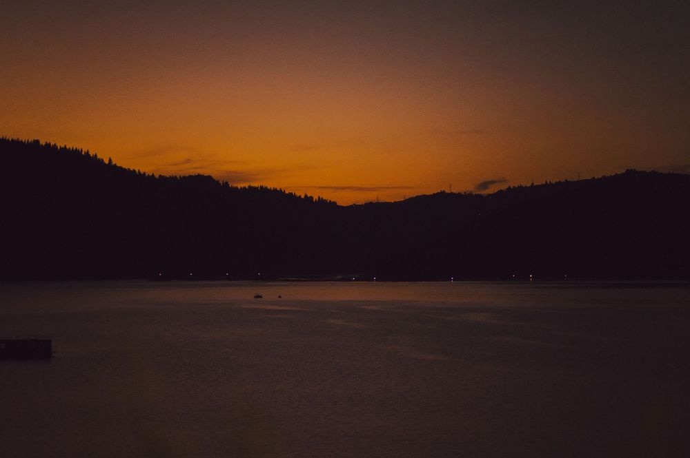 Scenic sunset over a lake with silhouetted mountains and an orange sky.