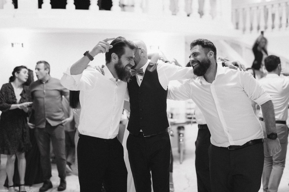 Three men laughing and celebrating together at a joyous gathering in black and white.