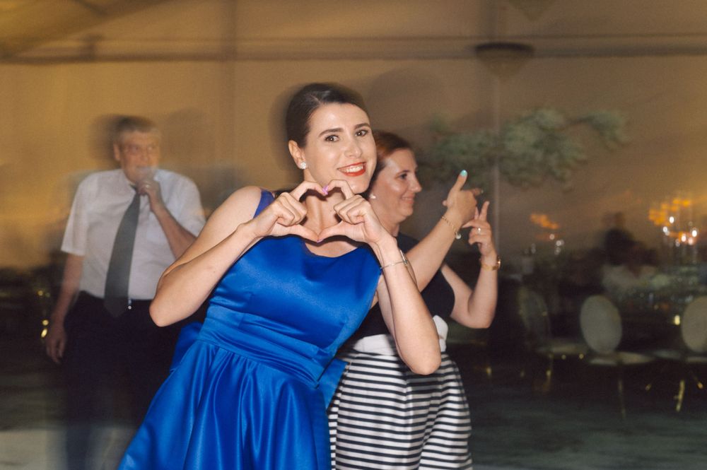 Woman in blue dress making heart shape gesture while dancing at a celebration.
