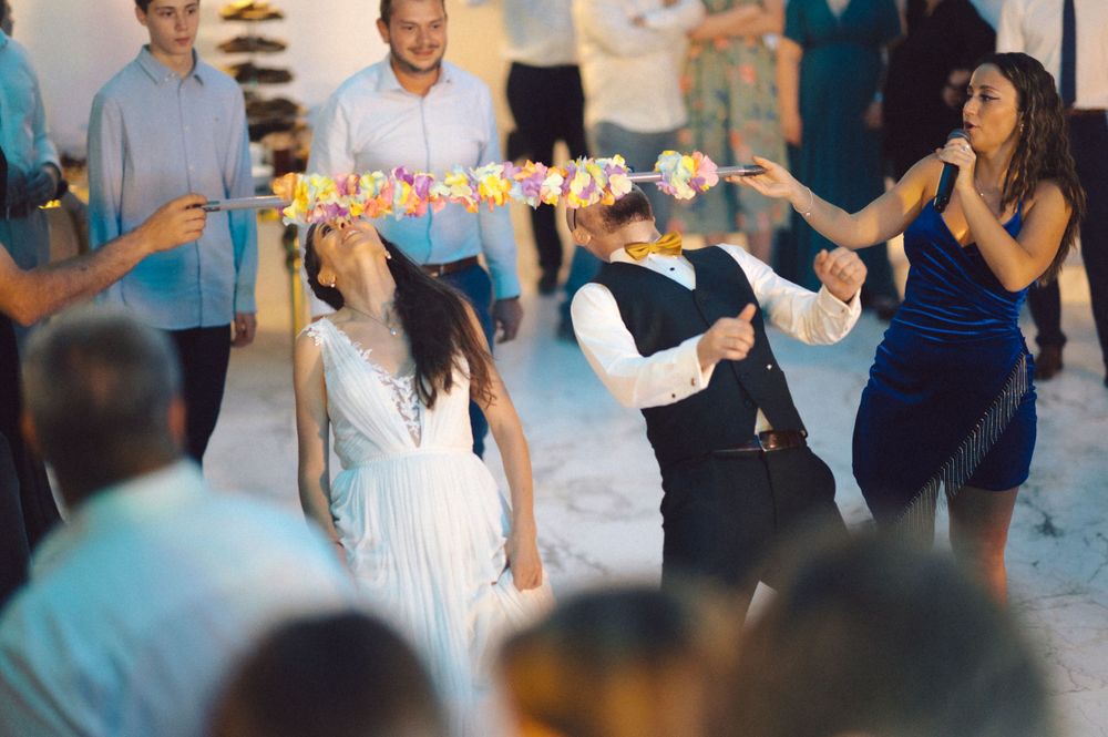 Wedding guests dancing in line while holding colorful flower garlands at reception.